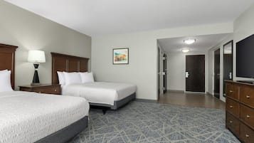 A hotel room with two beds, a desk, a lamp, a painting, and a wardrobe.