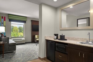 Habitación de hotel con kitchenette, un espejo grande, una ventana con vistas a árboles, un sofá y una silla.