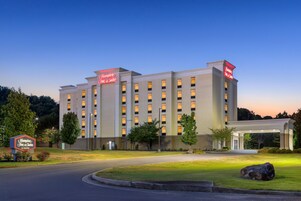 Um hotel Hampton Inn & Suites com fachada moderna, várias janelas e um gramado bem cuidado.