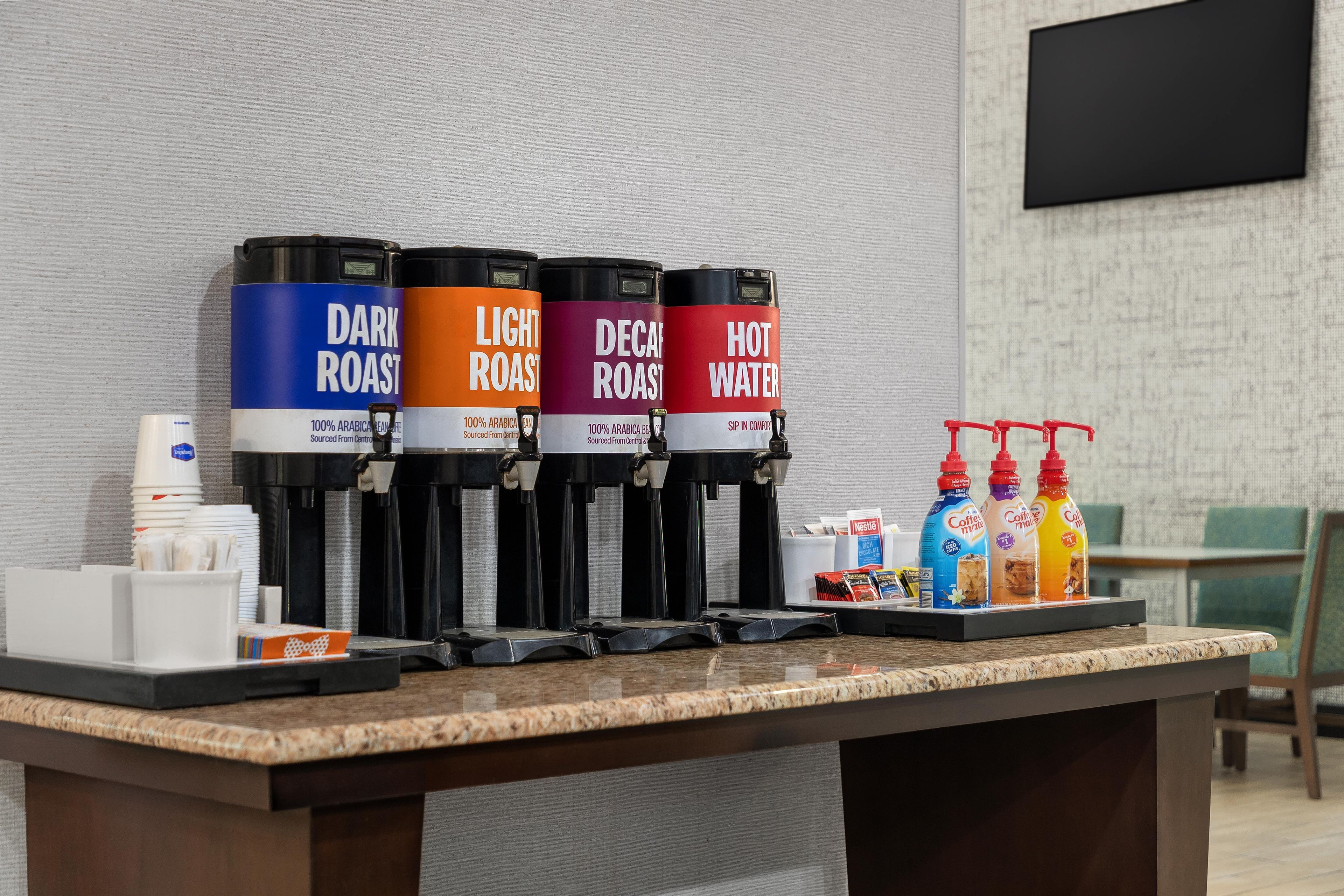 Estación de café con cuatro dispensadores etiquetados como tostado oscuro, tostado claro, descafeinado y agua caliente.