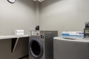 Uma lavanderia com máquina de lavar, secadora e um porta-toalhas com toalhas dobradas.