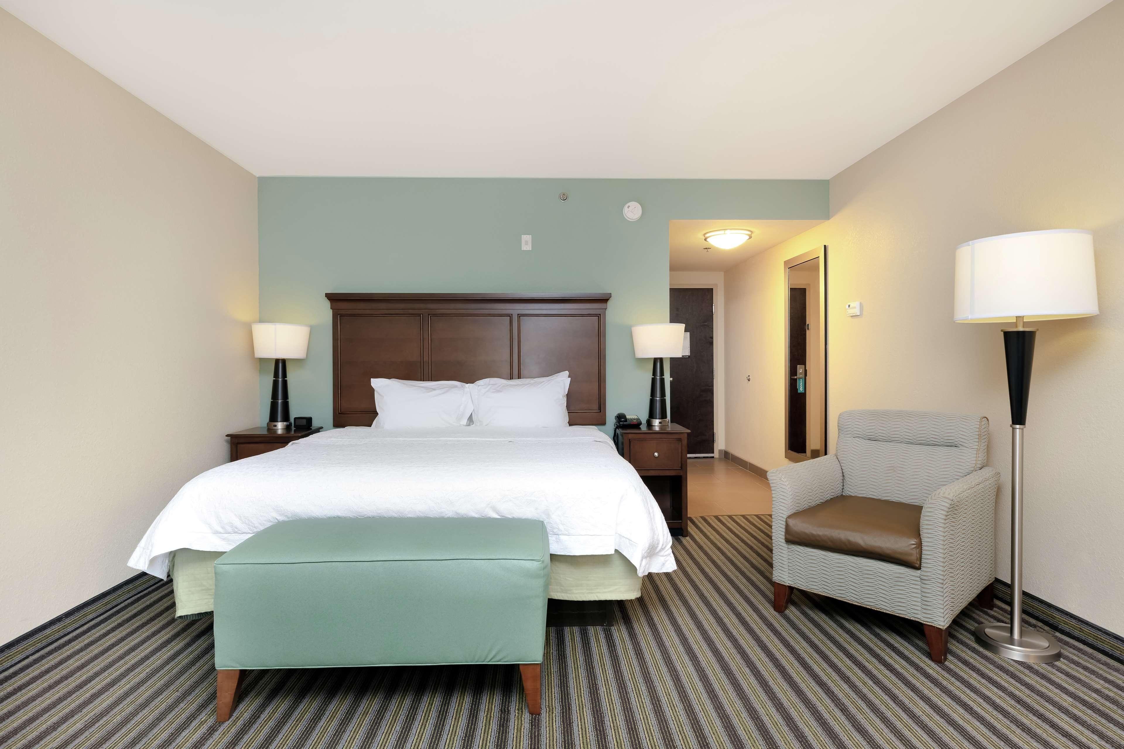 A hotel room with a bed, a nightstand, a chair, a bench, and a floor lamp.