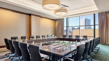 A conference room with a long table, multiple chairs, and a city view through large windows.