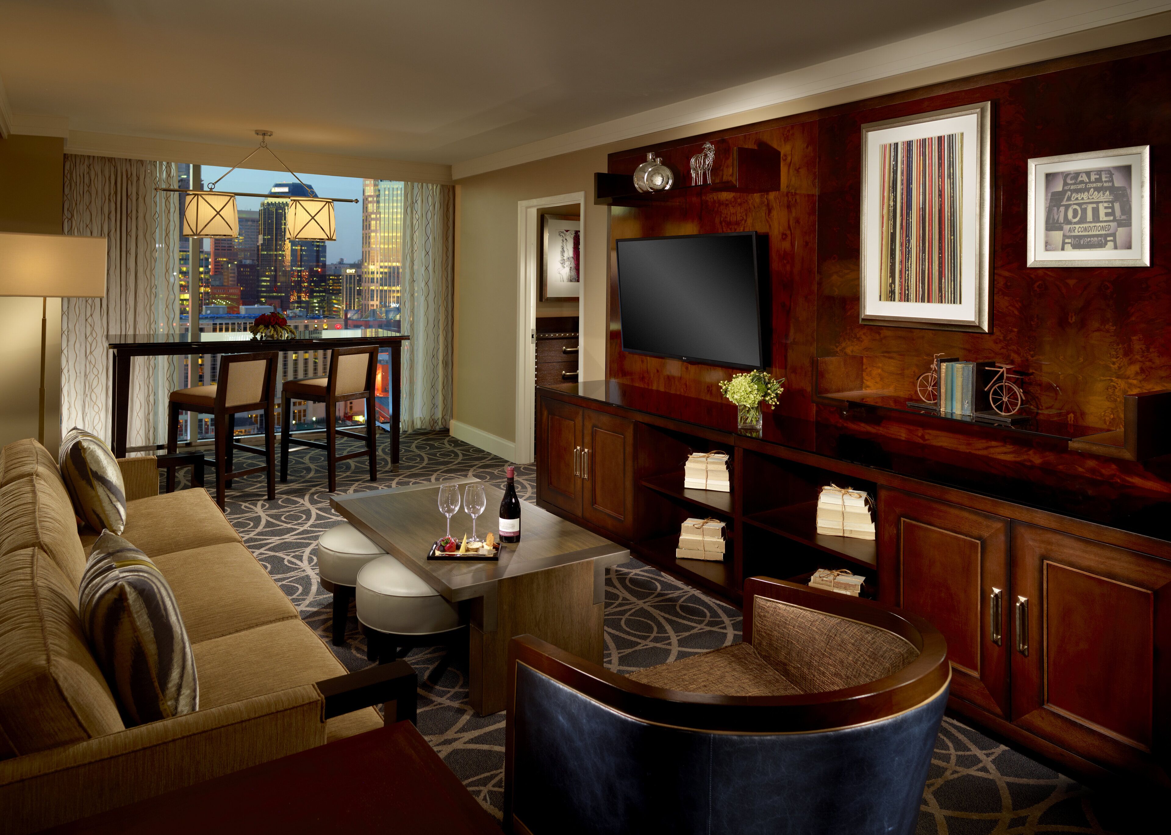 A hotel room with a city view, a dining area, a living room with a TV, and a minibar.