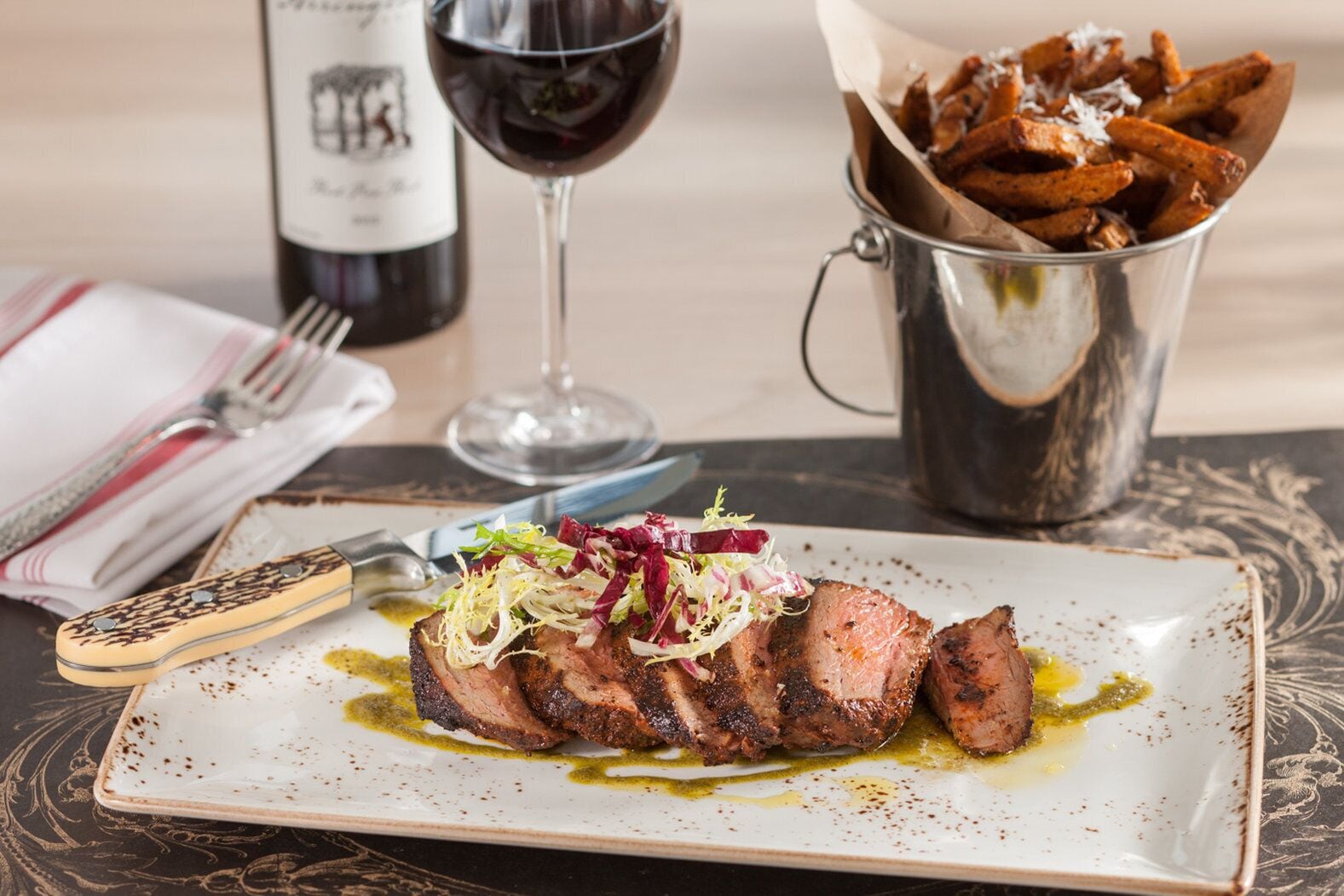 Une assiette de steak accompagnée de frites et d’un verre de vin rouge.