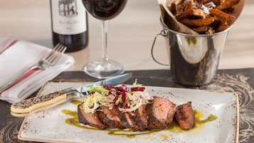 Une assiette de steak accompagnée de frites et d’un verre de vin rouge.