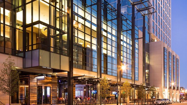 Un hotel moderno con fachada de vidrio, asientos al aire libre y una entrada destacada.