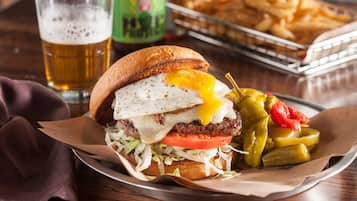 A burger with a fried egg, cheese, and pickles, served with fries and a drink.
