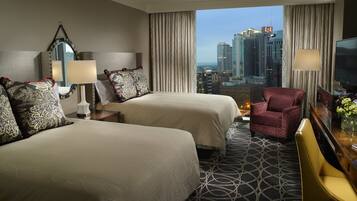 A hotel room with two beds, a TV, a chair, and a view of the cityscape.