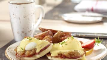 A plate of eggs Benedict with bacon and hollandaise sauce, accompanied by a cup of coffee and croissants.