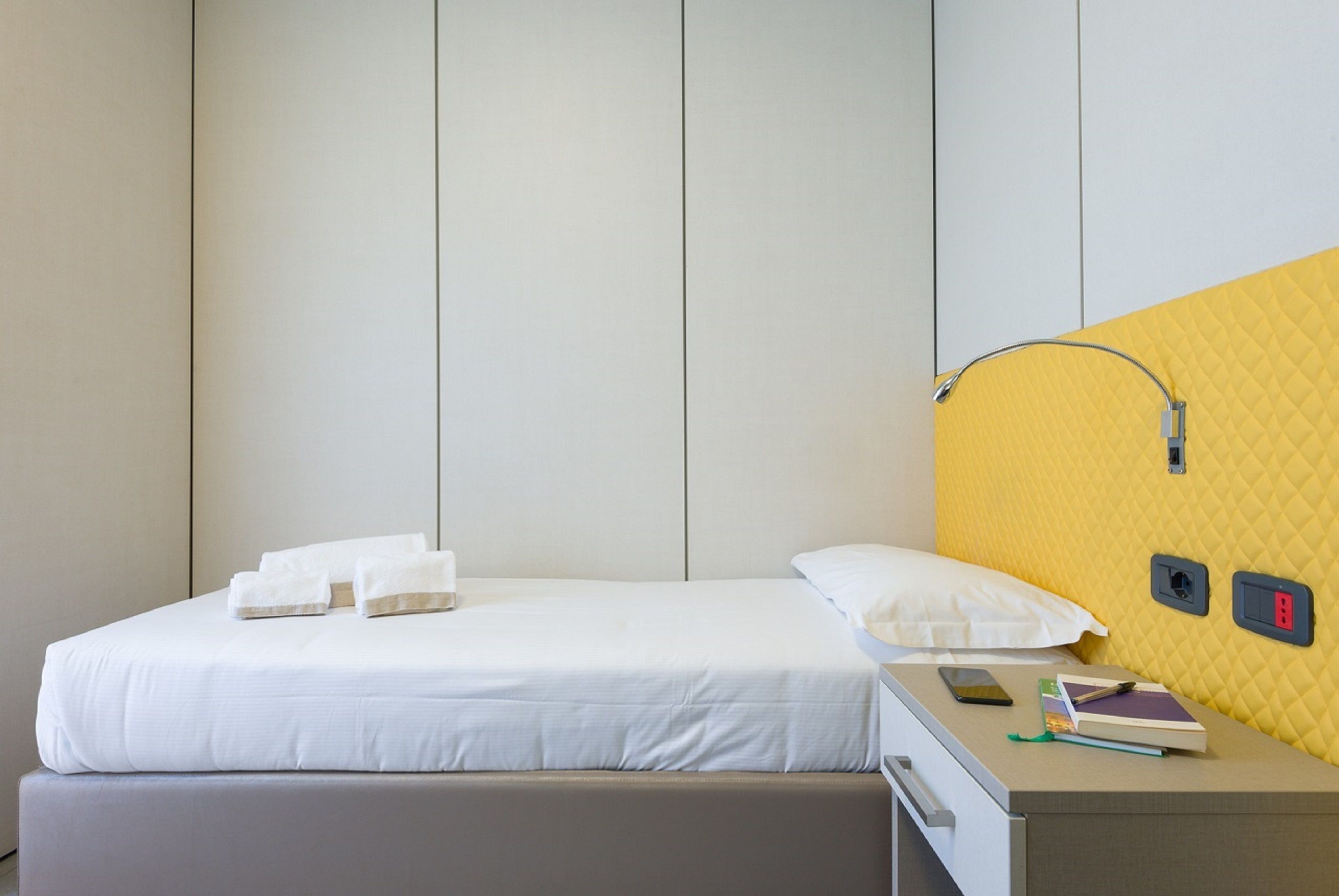Una habitación de hotel con cama, mesita de noche y pared de acento amarilla.