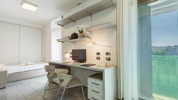 A modern, minimalist bedroom with a bed, bedside table, and a large window offering a city view.