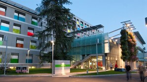 Un edificio moderno con fachada de vidrio, un cartel verde que indica una dirección y una escalera que lleva a un nivel superior.