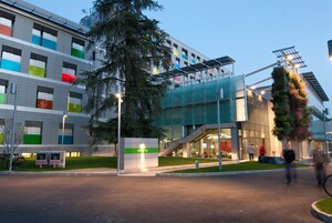 Un edificio moderno con fachada de vidrio, un cartel verde que indica una dirección y una escalera que lleva a un nivel superior.