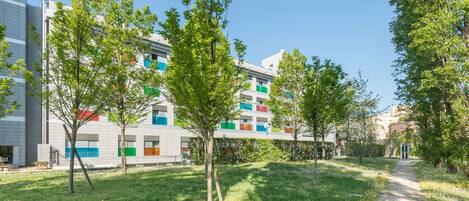 A pathway leading to a modern building with colorful windows, surrounded by green trees and grass.