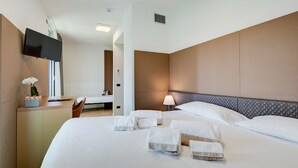 Una habitación de hotel con una cama grande, un escritorio con ordenador, un televisor montado en la pared y una lámpara de noche.