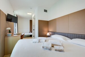 A hotel room with a large bed, a desk with a computer, a TV mounted on the wall, and a bedside lamp.