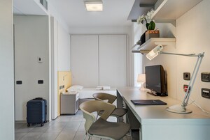 Habitación de hotel moderna con cama, escritorio, sillas, lámpara de escritorio, televisor y maleta.