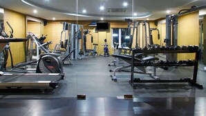 A gym with cardio machines, weight benches, and free weights. - Quality Inn Viha (Kumbakonam)