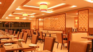 A restaurant with multiple tables and chairs, warm lighting, and decorative panels. - Quality Inn Viha (Kumbakonam)