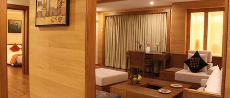 A modern hotel room with a wooden interior, a dining area with a table and chairs, and a seating area with sofas and a coffee table.