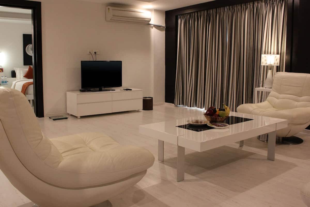 A modern living room with a white sofa, a coffee table with fruit, a flat-screen TV on a white cabinet, and a striped curtain.