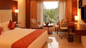 A hotel room with a large bed, two armchairs, a desk, and a view of greenery through the window. - Quality Inn Viha (Kumbakonam)