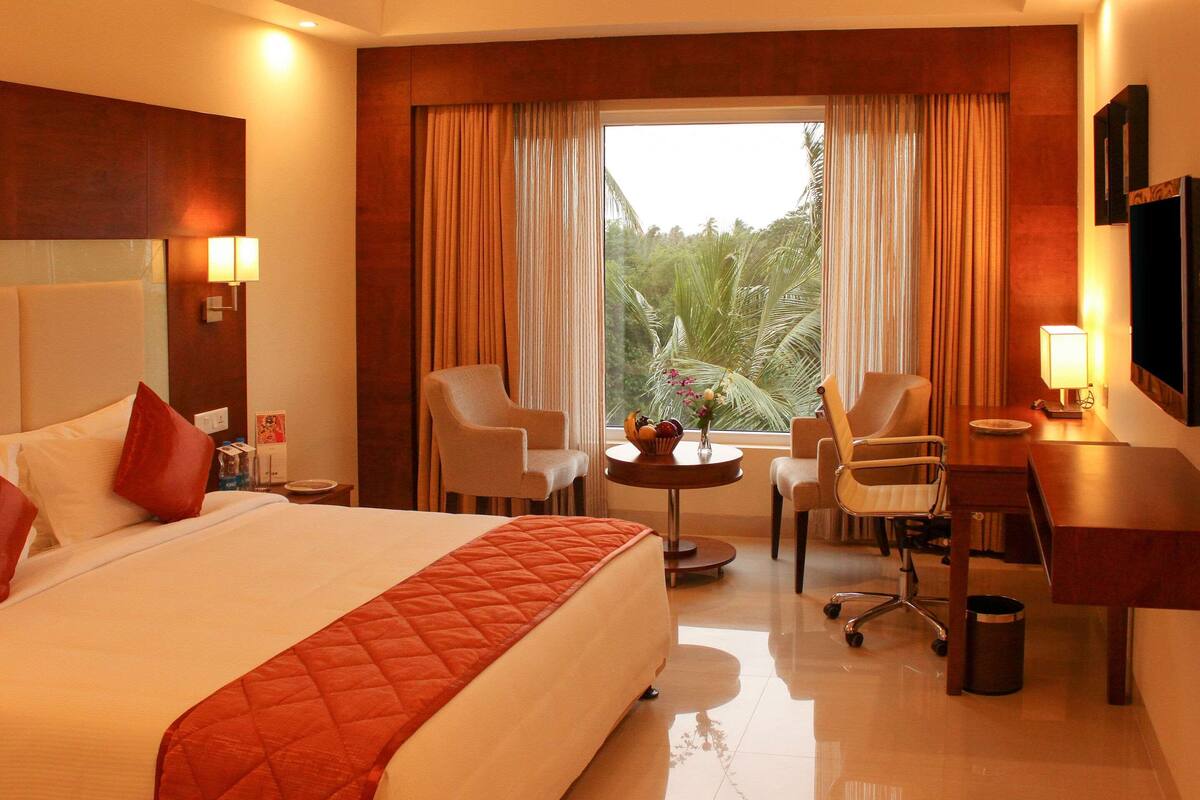 A hotel room with a large bed, two armchairs, a desk, and a view of greenery through the window.