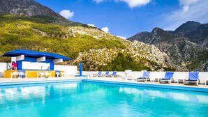 A swimming pool with lounge chairs and a covered seating area, surrounded by mountains.
