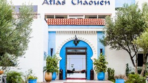 The exterior of Hotel Atlas Chaouen with a blue door, white walls, and red-tiled balconies.