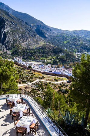 Restaurante com área externa e mesas apreciando uma paisagem montanhosa.