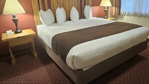 Una habitación de hotel con una cama grande, dos mesitas de noche con lámparas, un cabecero de madera y una ventana con cortinas.