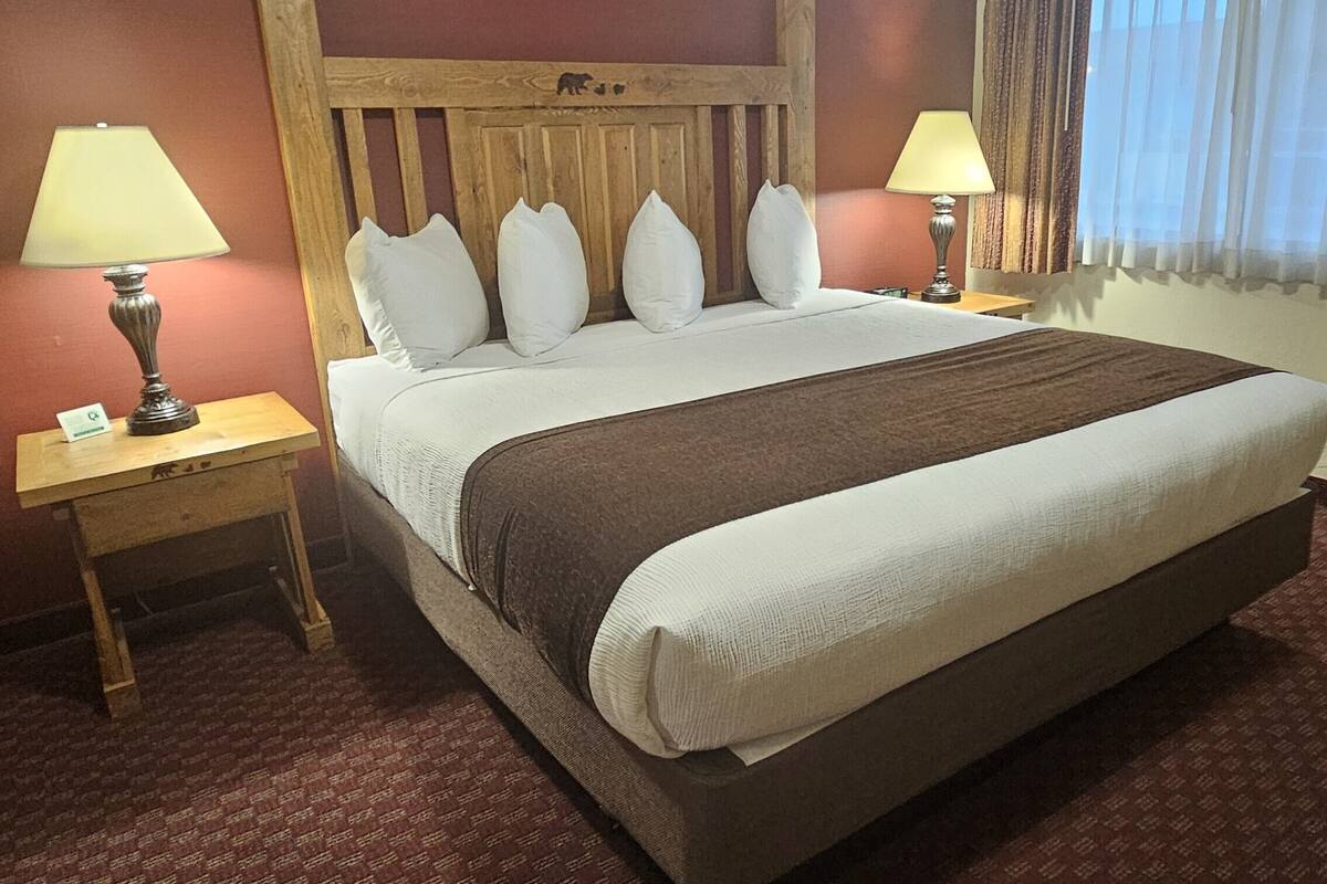 A hotel room with a large bed, two bedside tables with lamps, a wooden headboard, and a window with curtains.