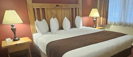 Una habitación de hotel con una cama grande, dos mesitas de noche con lámparas, un cabecero de madera y una ventana con cortinas.