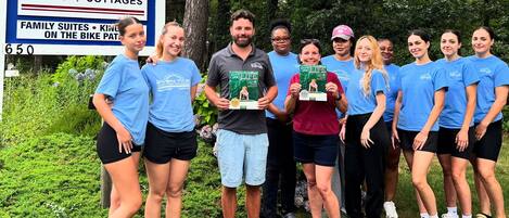 A group of people standing in front of a sign for Ven'tide Rooms & Cottages, indicating family suites and a bike path.