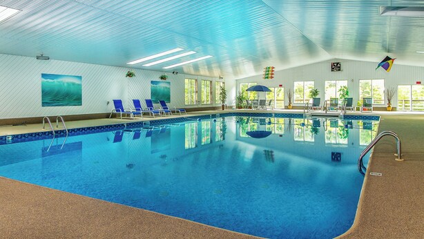 An indoor swimming pool with clear blue water, lounge chairs, and potted plants. - The Even'tide (Wellfleet)