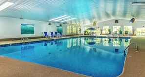 An indoor swimming pool with clear blue water, lounge chairs, and potted plants. - The Even'tide (Wellfleet)