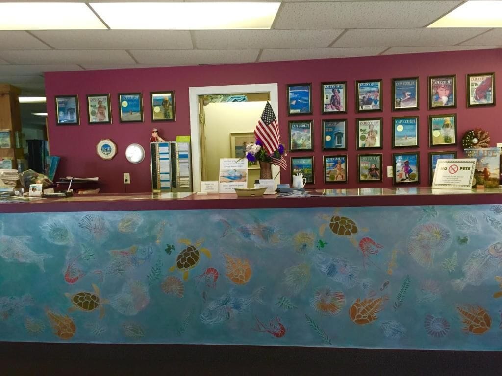 Zona de recepción con pared morada, carteles enmarcados, una vitrina de vidrio y un mostrador azul con diseño.