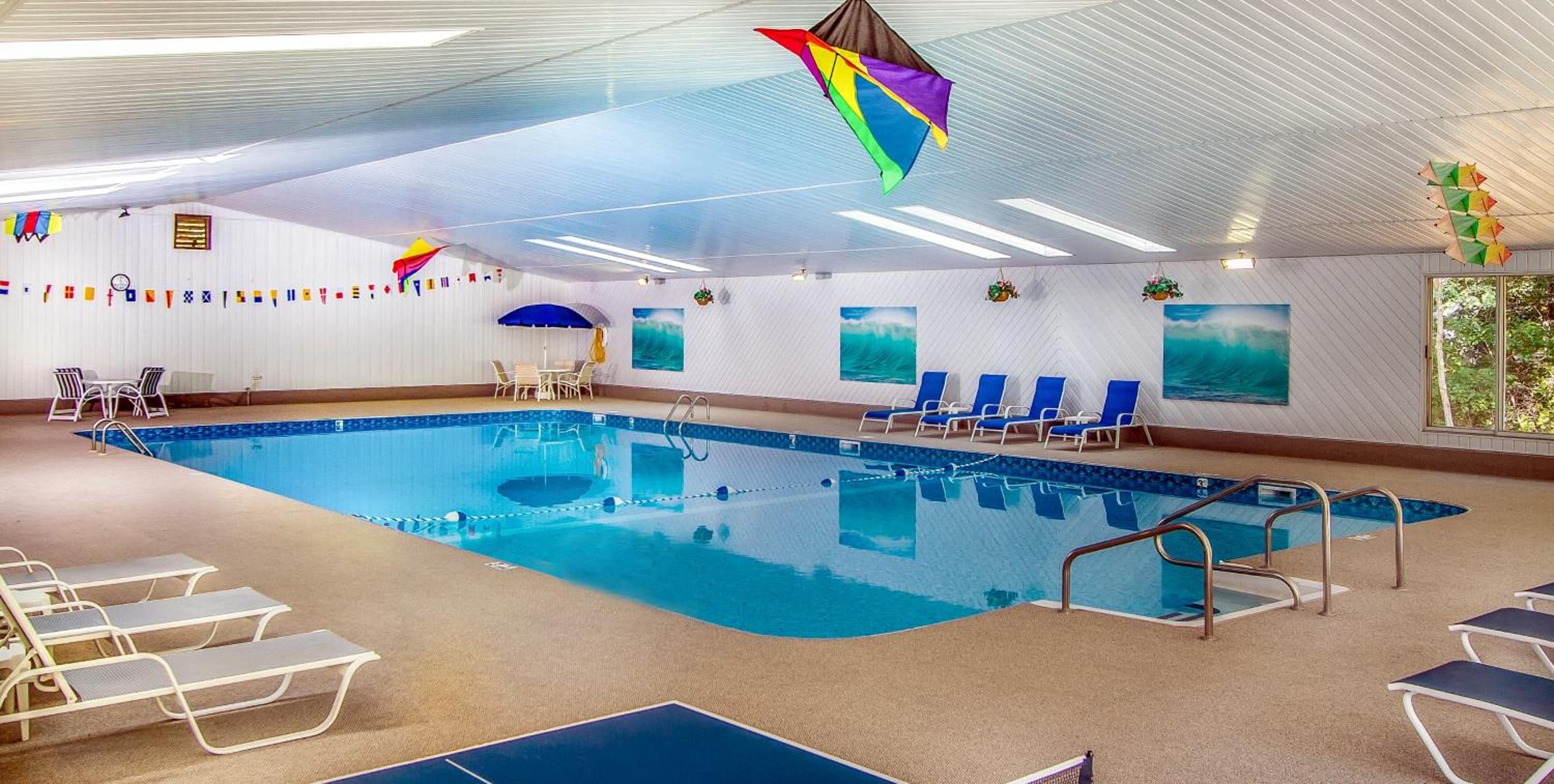 Una piscina interior con sillas de descanso, una zona de camas sol y un techo con una cometa colgante.