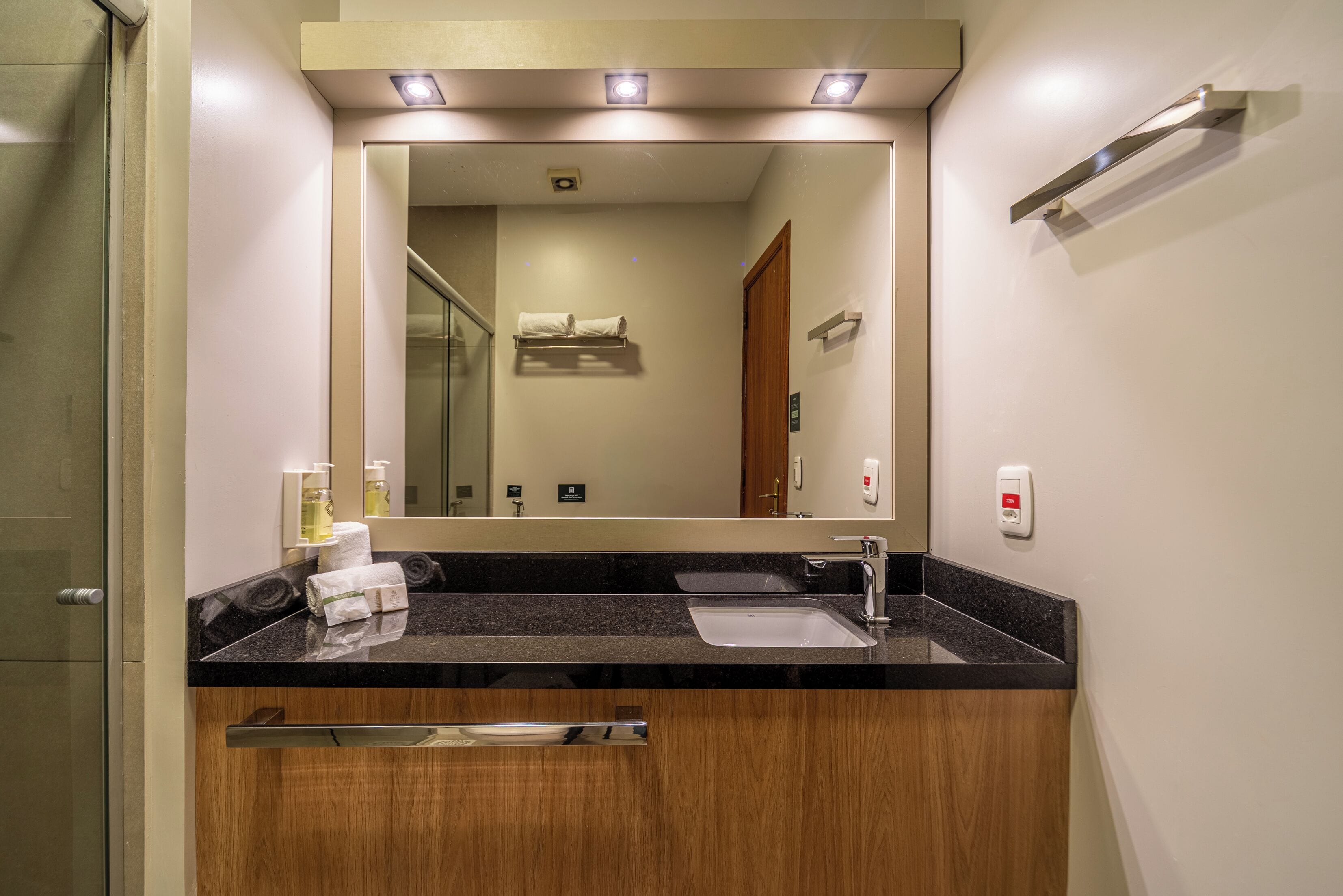 A modern bathroom with a large mirror, a sink, a towel rack, and a wooden vanity.