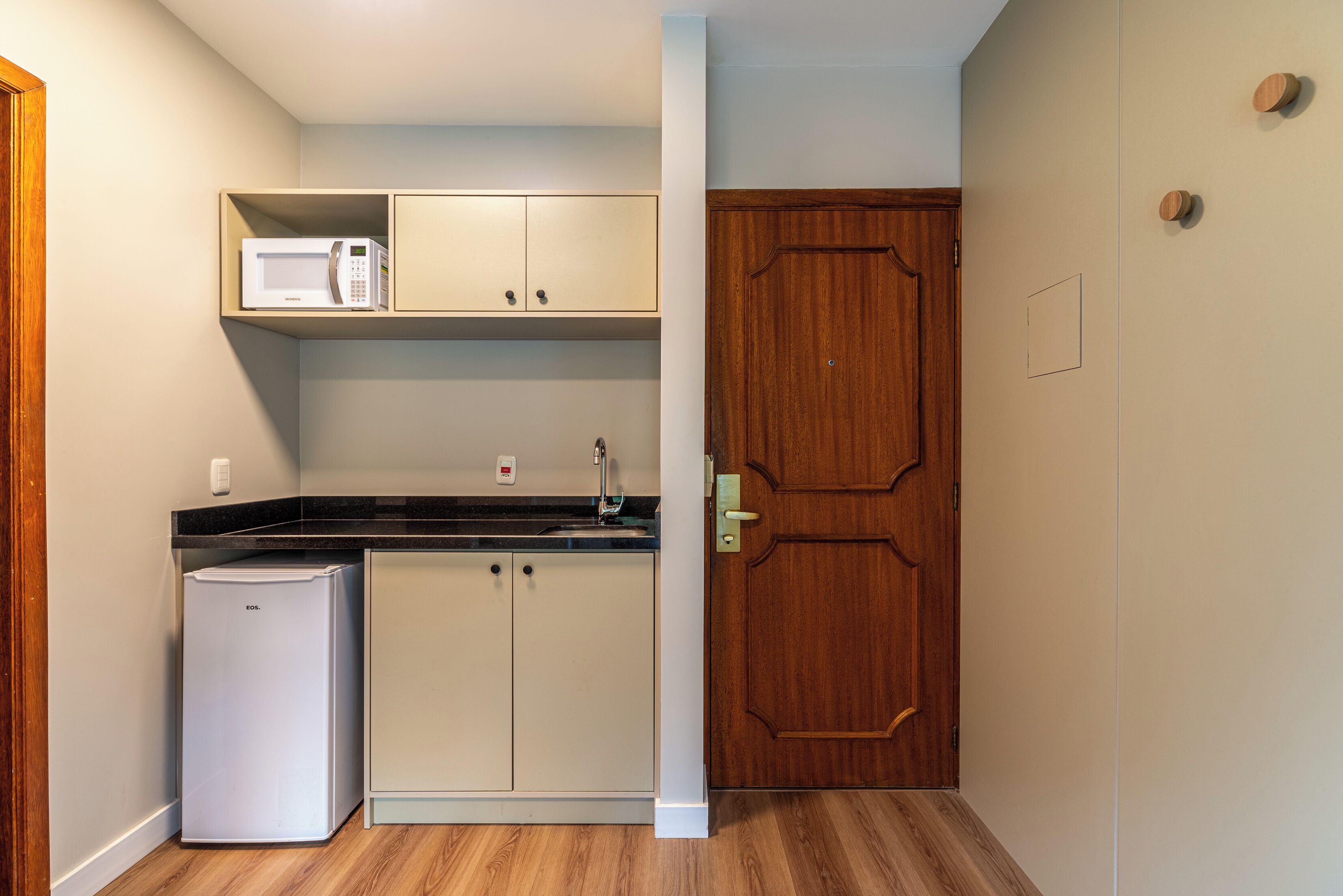 Una cucina compatta con forno a microonde, frigorifero e porta in legno.