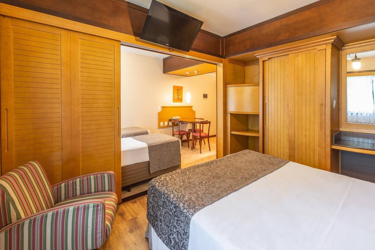 Una habitación de hotel con una cama, un sofá a rayas, un escritorio con silla y armarios de madera.