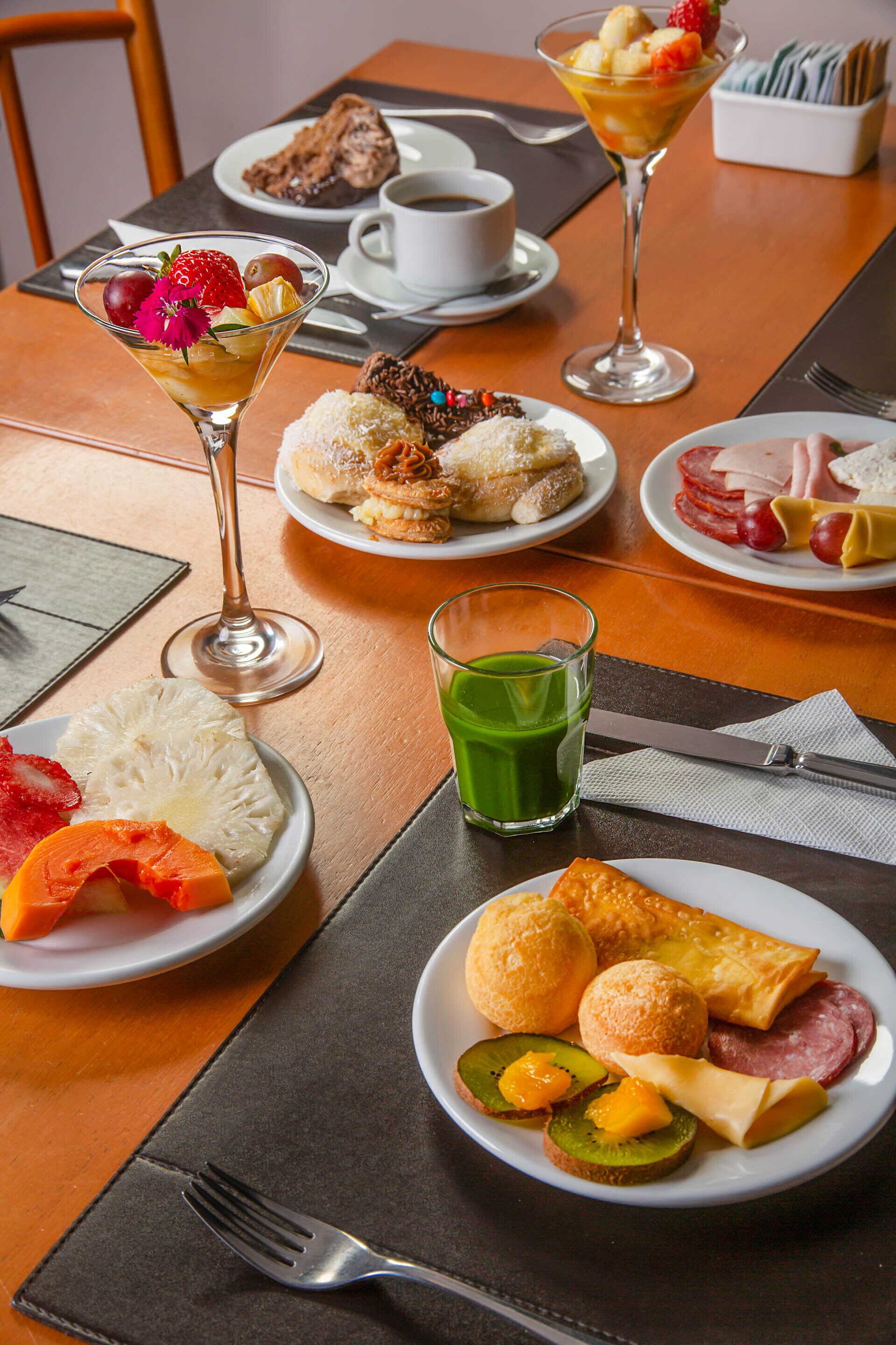 A dining table with various dishes, including a fruit salad in a glass, a plate with bread and cheese, and a cup of coffee.