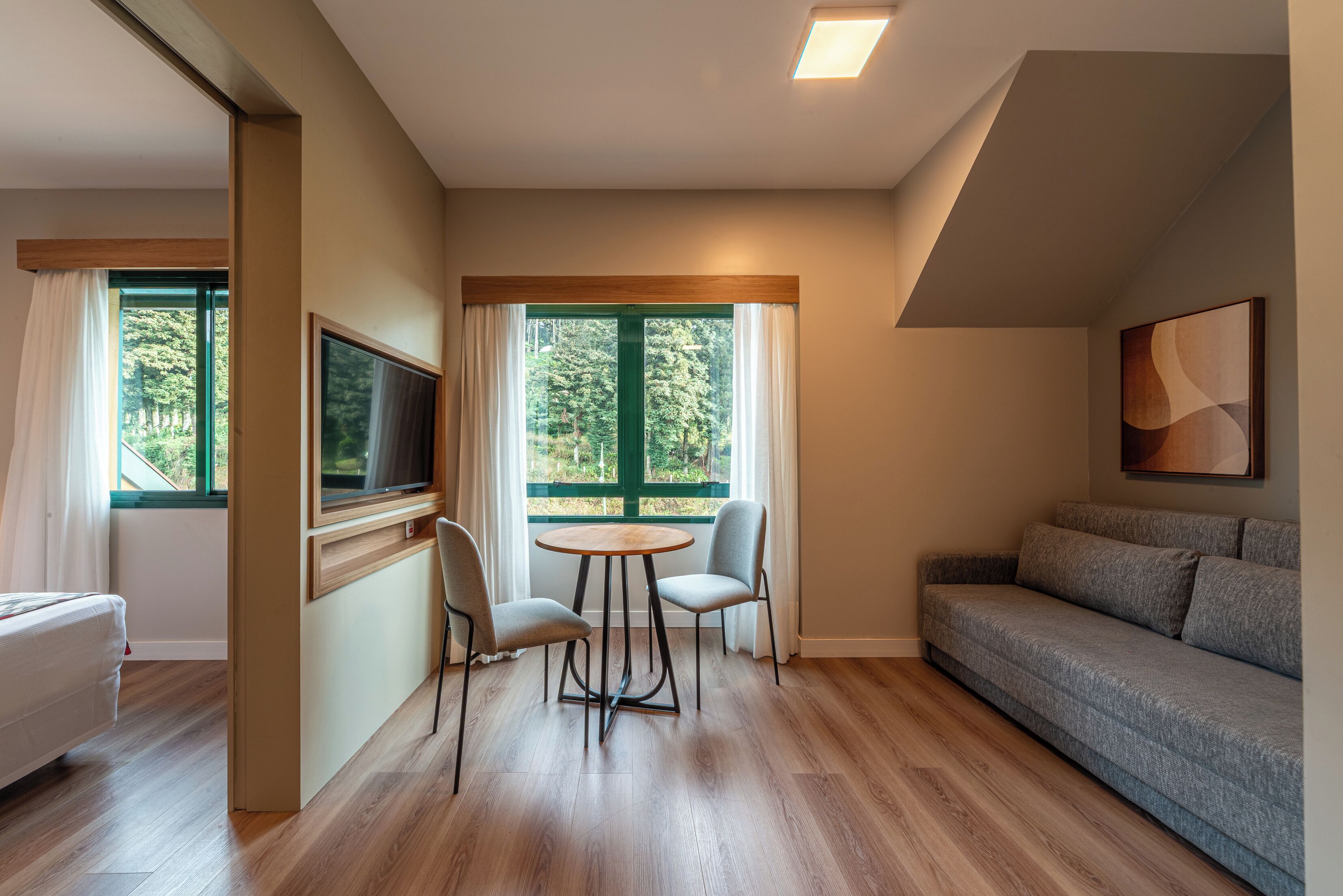 Una sala de estar moderna con un sofá, un televisor, una mesa de comedor con sillas y ventanas amplias con cortinas.