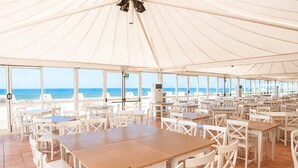 A covered outdoor dining area with tables and chairs, large windows offering a view of the sea, and an air conditioning unit. - La Plage Resort (Sorso)