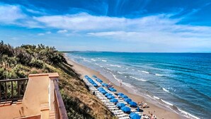 A beach with rows of sun loungers and blue umbrellas, a wooden deck, and a view of the ocean. - La Plage Resort (Sorso)