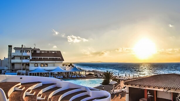 A resort with a pool, lounge chairs, and a view of the sea at sunset. - La Plage Resort (Sorso)