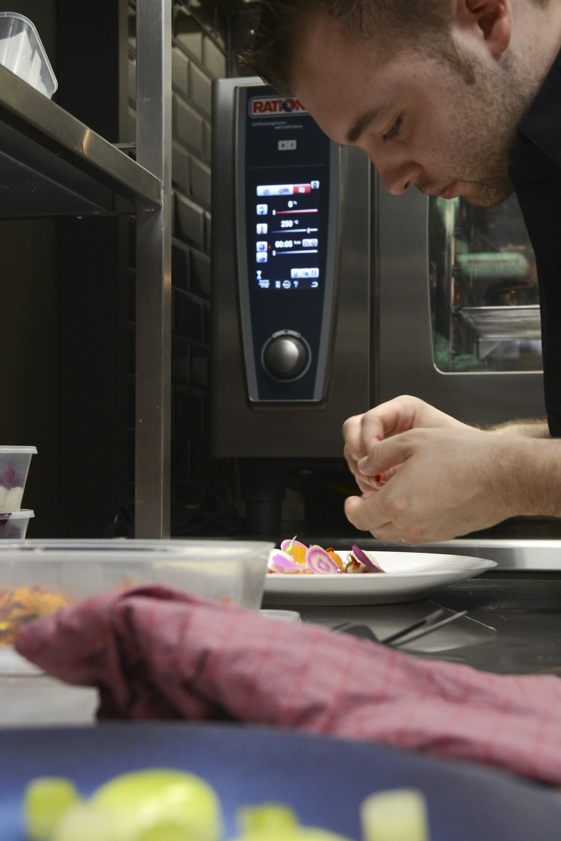 A person working at a counter with a digital display, a plate of food, and a cup.
