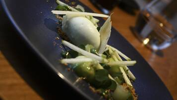 A dessert plate with a spherical white item, green leaves, and a dark blue plate.