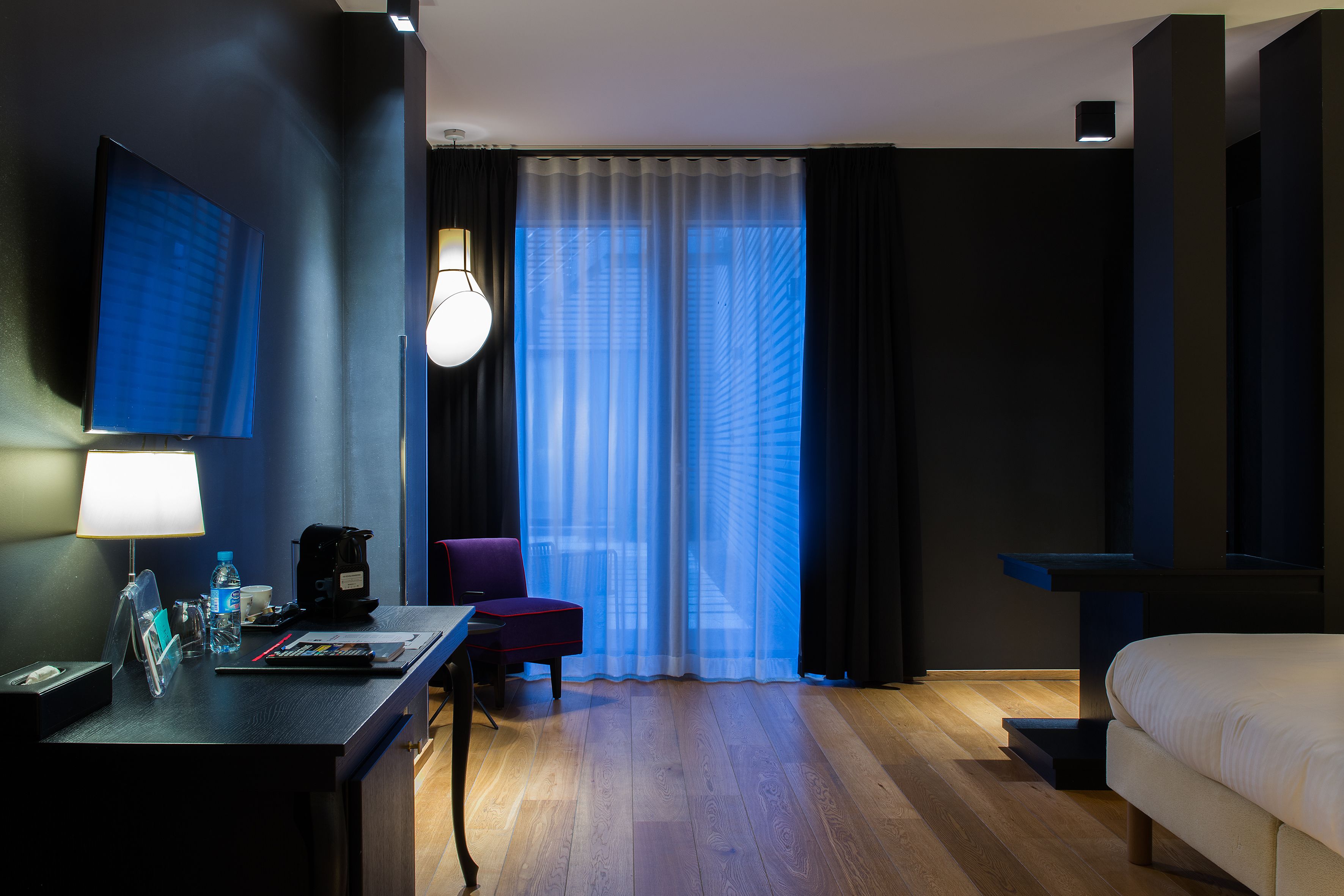 Una habitación de hotel con escritorio, silla, cama y un ventanal con cortinas.
